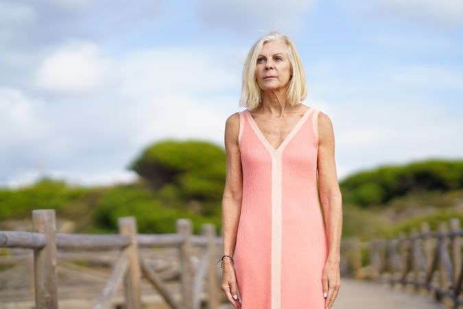 Serious older woman with grey hair standing on wooden walkway near the coast, copy space
