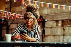 Happy Black woman in stripe shirt texting on phone in cafe