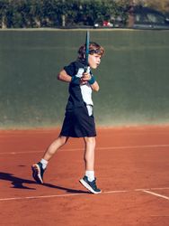 Sporty kid in activewear playing tennis with racket on court