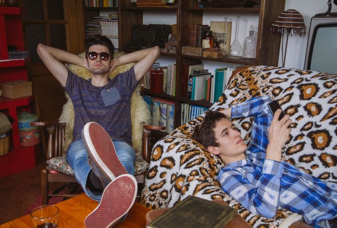 Young man looking smartphone lying and friend relaxing in rocking chair