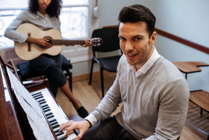 Man playing piano near woman playing guitar in studio