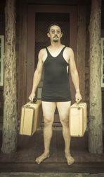Gentleman Dressed in 1920’s Era Swimsuit Holding Suitcases on Porch