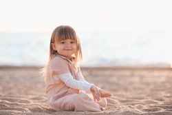 Girl in yellow outfit sitting on sandy beach