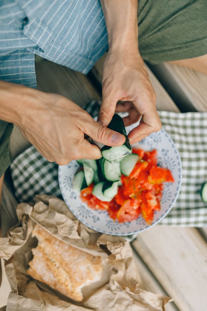 Top view of person sitting beside plate of tomato and cucumber beside loaf of bread