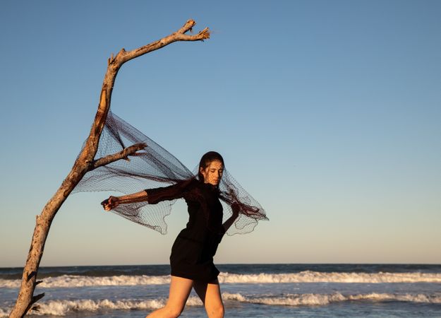 Woman in fishing net fixed on twig near water on shore