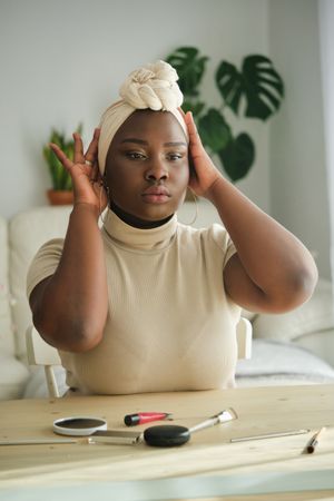 Black lady adjusting headscarf in front of mirror