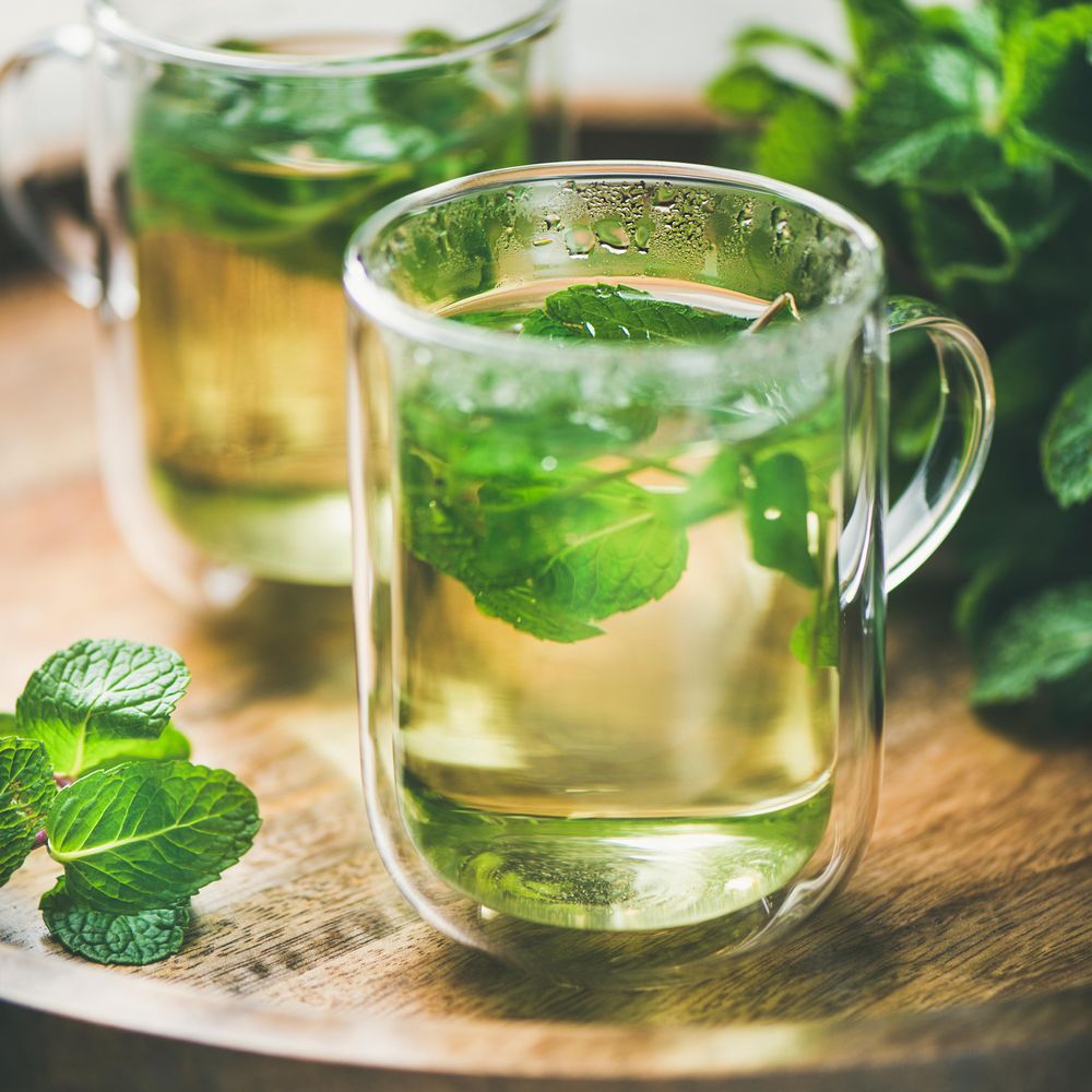 Close up of mint tea with fresh mint leaves on wooden tray, square crop