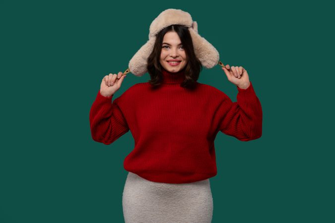 Smiling woman in red sweater adjusting fluffy fur hat