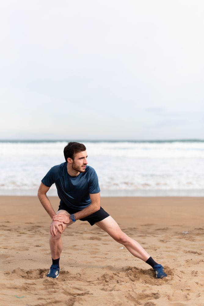 Male athlete in active wear doing exercises on legs at empty beach