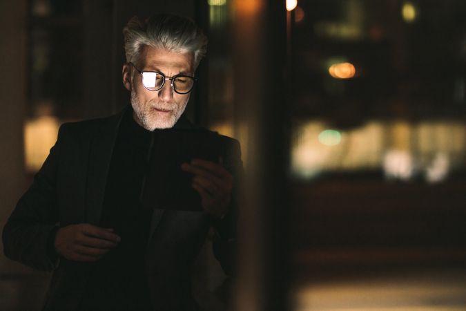 Businessman with gray hair looking at digital tablet in office at night
