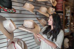 A young Hispanic woman is choosing a hat in a shop