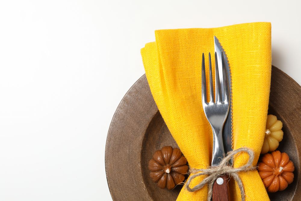Cutlery with yellow napkin on wooden plate on light background, close up