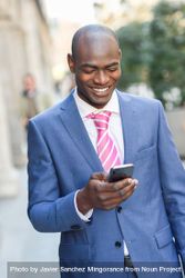 Smiling male in business attire looking down at phone and texting outside 5k2mo0
