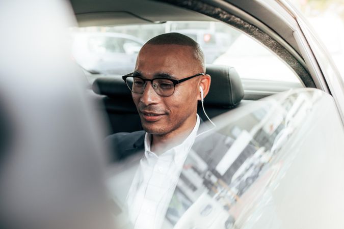 Business person wearing eyeglasses sitting in his sedan on back seat going to office