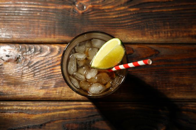Glass with ice cola and lime slice on wooden background