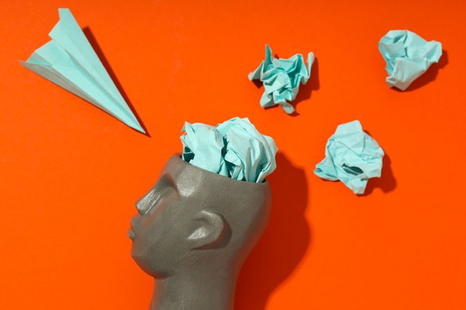 Side of grey bust of head on red background with paper airplane, close up