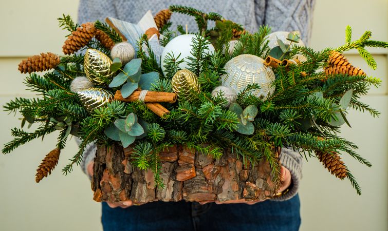 Person holding Christmas wooden centerpiece with pine and baubles