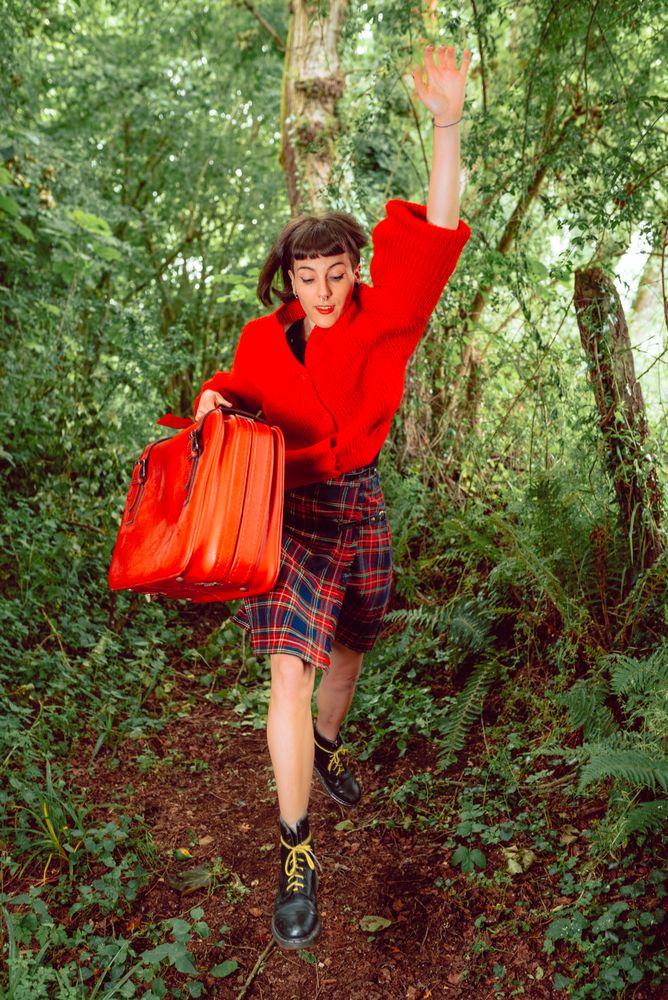 Woman in red with big red suitcase in forest