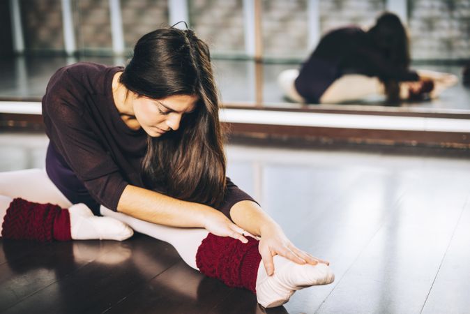Young woman practicing ballet and flexing muscles sitting on studio floor.