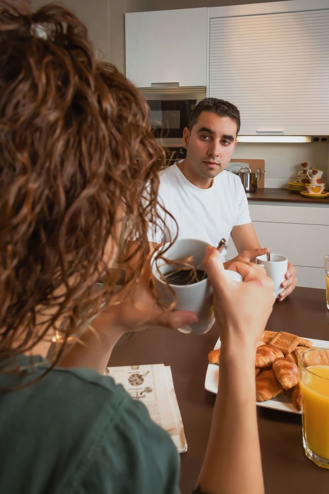 Serious couple talking while eating pastries and drinking coffee at breakfast