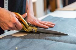 Close-up of fashion designer hands using scissors to cut textile at work table