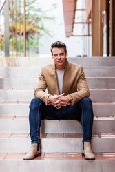 Man in jeans and autumn coat sitting down on outdoor staircase smiling at camera