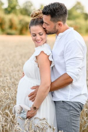 Happy pregnant couple hugging in field