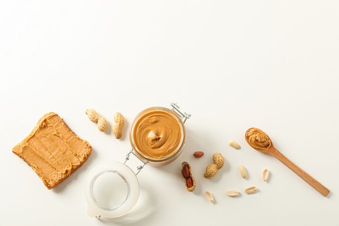 Flat lay composition with peanut butter sandwich, glass jar, peanut and spoon on light background, space for text