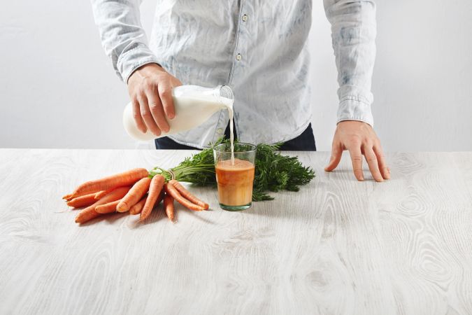 Man pouring milk into carrot juice
