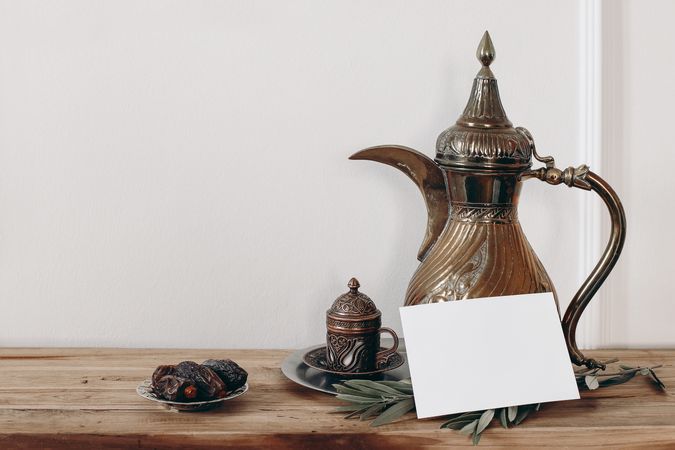 Arabic dallah coffee pot and blank greeting card mockup on wooden table