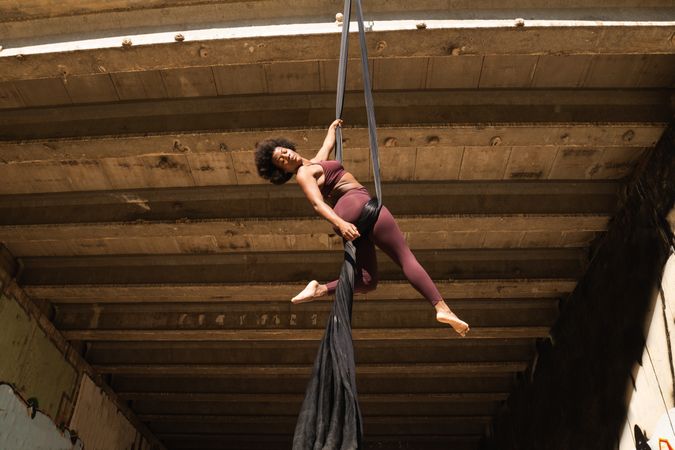Slim woman doing yoga with aerial silks in city
