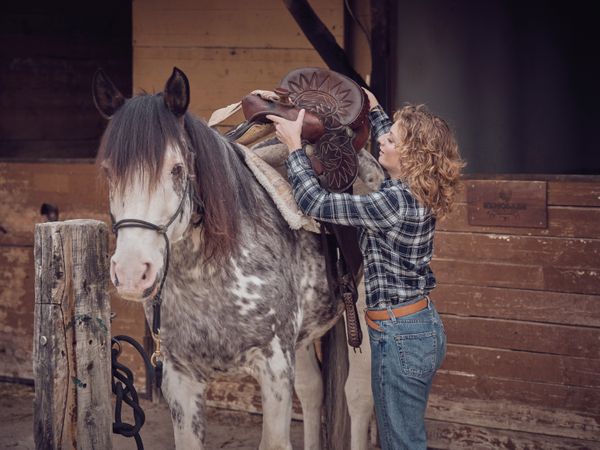 Woman putting on saddle on horse