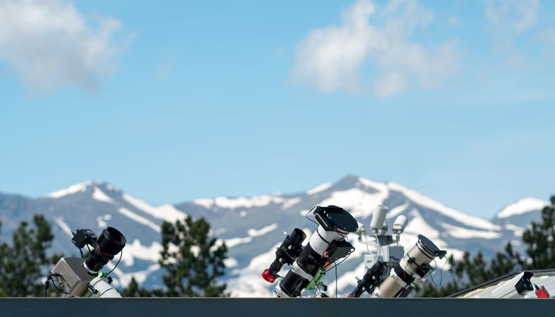 Telescopes on rooftop with snow-covered mountains in background.