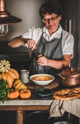 Woman with short hair and glasses grinding pepper onto soup in cozy kitchen