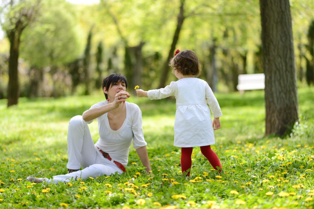 Woman with daughter playing with flowers in sunny park