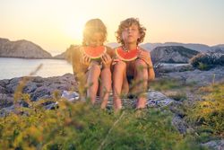 Happy siblings eating watermelon on seashore