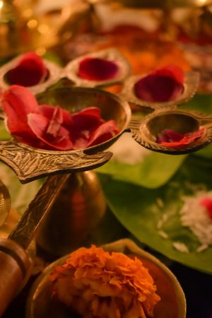 Rose petals on golden panch aarti beside green leaves on a table