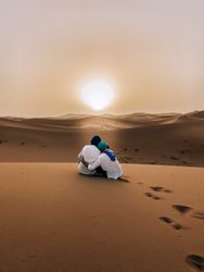 Back view of man and woman hugging and sitting on sand dune at sunset