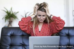 Young white woman using laptop at home sitting on the sofa scared and amazed with hands on head 5aXEqQ