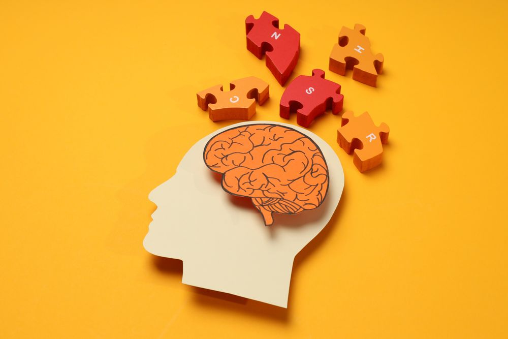 Paper cut out of head with brain & puzzle pieces on orange background
