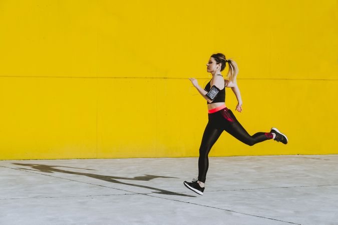 Woman with earphones running near wall