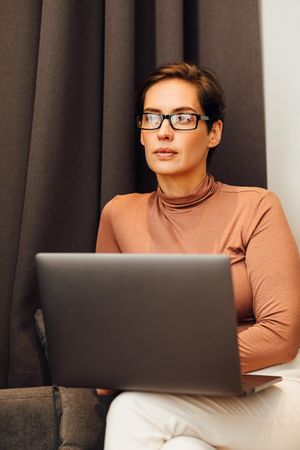 Woman in smart casual thinking while using her laptop