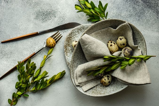 Easter card concept with top view of elegant grey ceramic bowl with speckled eggs and green branches