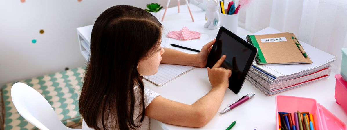 Girl studying at home with tablet and mask on table