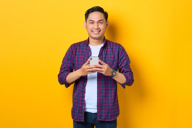 Smiling Asian in plaid shirt  holding smartphone