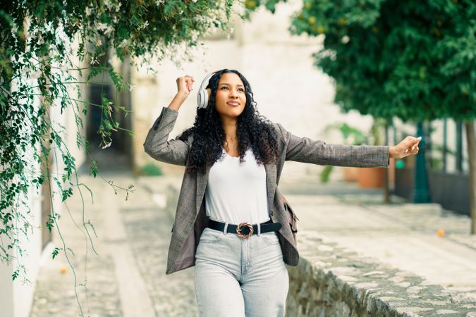 A Joyful Woman Dancing Outdoors While Wearing Headphones in a Beautiful, Charming Setting