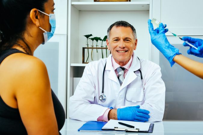 Medical assistant preparing injection for patient in smiling doctor’s office