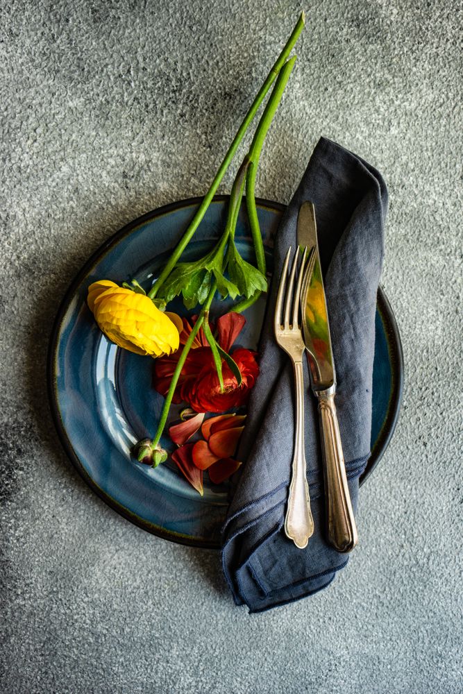 Top view of rustic table setting with red buttercup flowers on navy plate