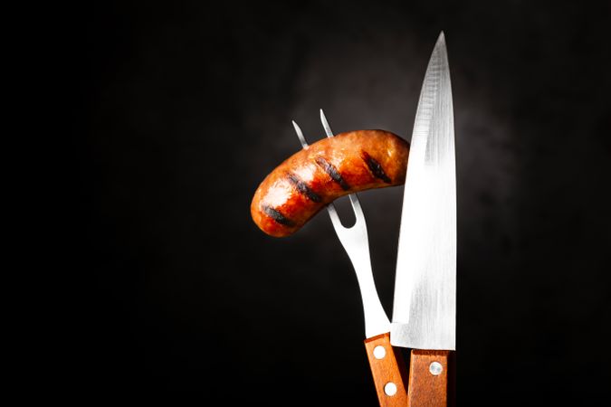 Fork piercing a grilled sausage and knife with space for text
