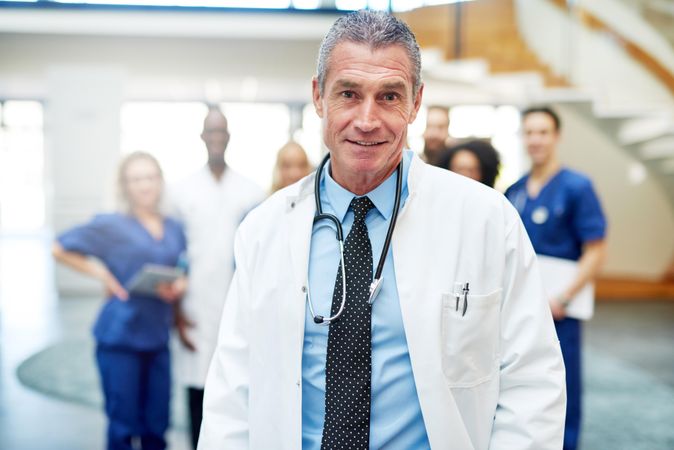 Portrait of mature doctor in lab coat and stethoscope with his medical team in the background
